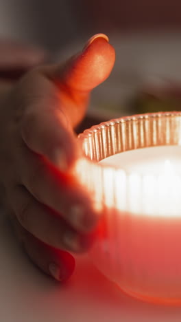 las manos de la mujer giran una vela encendida en un elegante soporte de vidrio sentada en la mesa durante una cena festiva en una habitación semi-oscura de primer plano extremo en cámara lenta