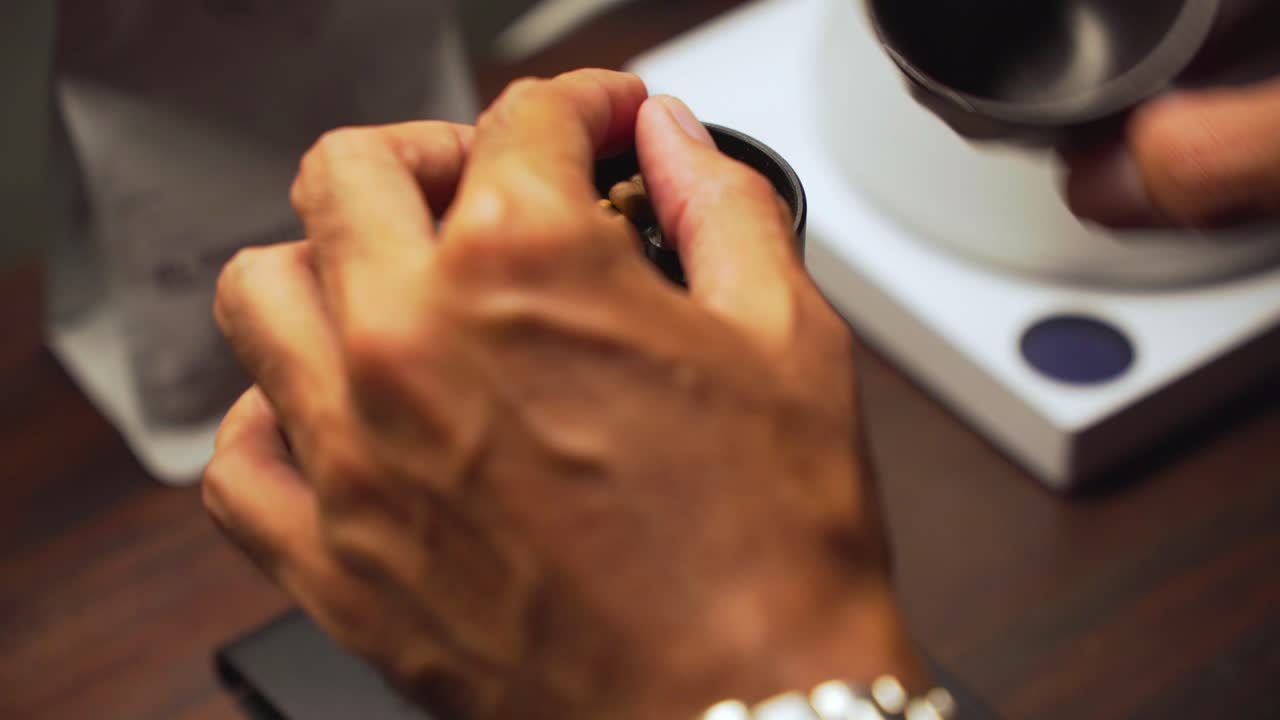 Barista menuangkan biji kopi hitam dalam jumlah tepat ke penggiling manual