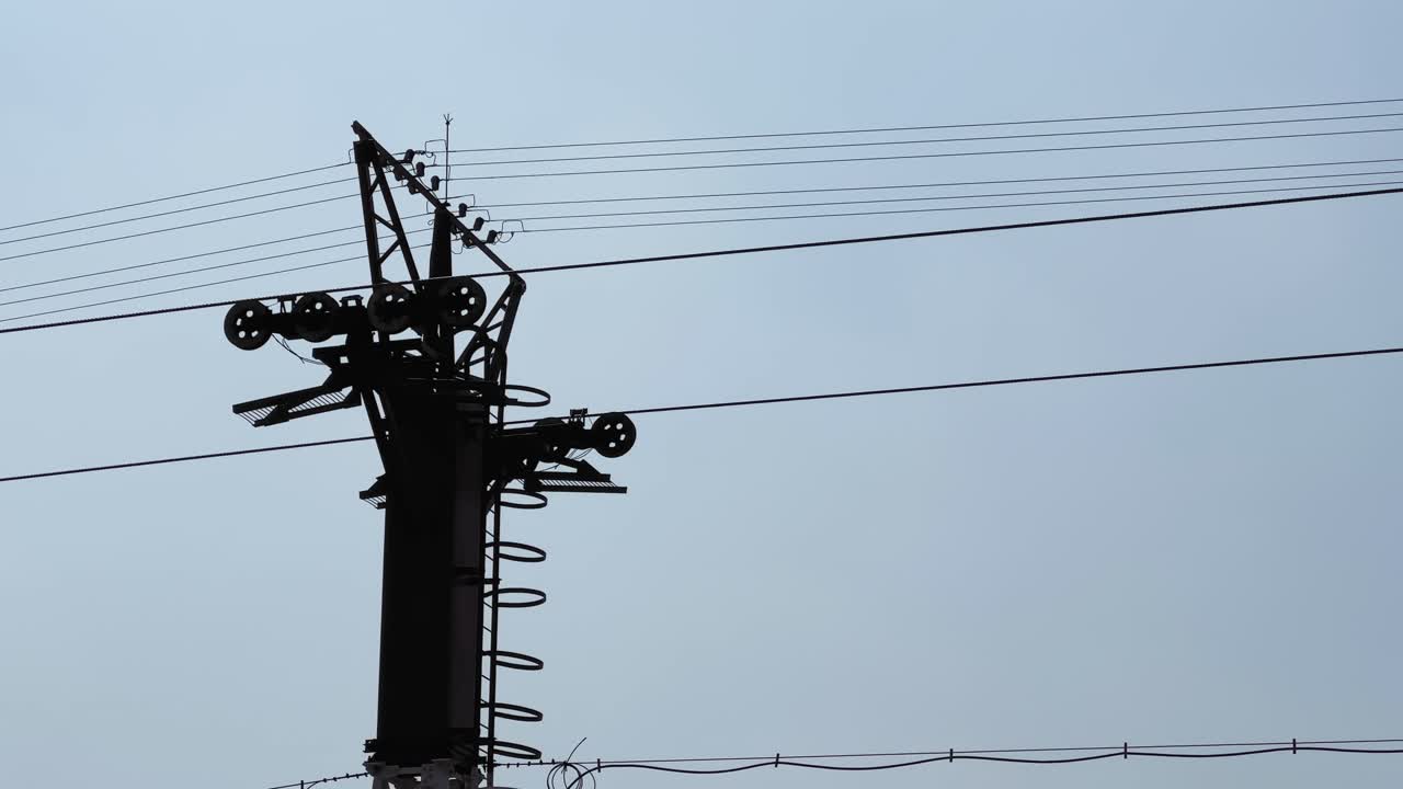 A static shot of a cable car support tower with pulleys and overhead cables in action silhouetted against a pale sky, highlighting transport and mechanical infrastructure
