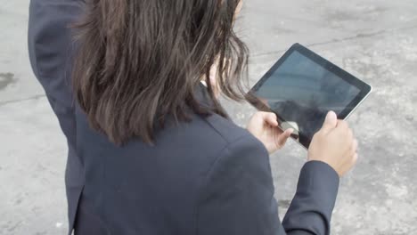 high angle of two female office colleagues using tablet and watching content together while walking outside