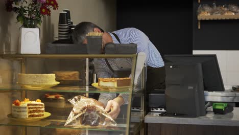 young handsome man vendor in the apron bringing fresh cake to the counter in the bakery shot. indoors