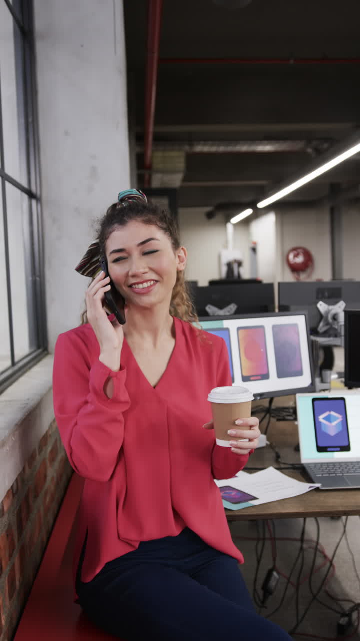 Vertical video of happy biracial female creative on smartphone at casual office, in slow motion