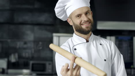 szef kuchni pozuje z rolką w kuchni. uśmiechnięty szef kuchni bawi się rolką.