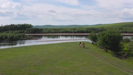 dos personas montando caballos a través de un paisaje idílico de prado verde junto a un río