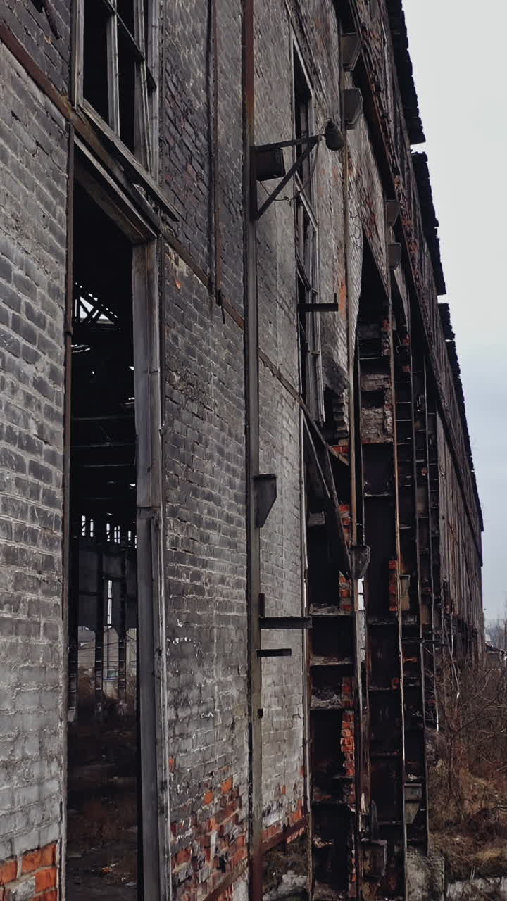Former plant building with damaged brick walls and metal structures covered with moss on the roof and overgrowths inside and outside. Aerial view. Vertical video