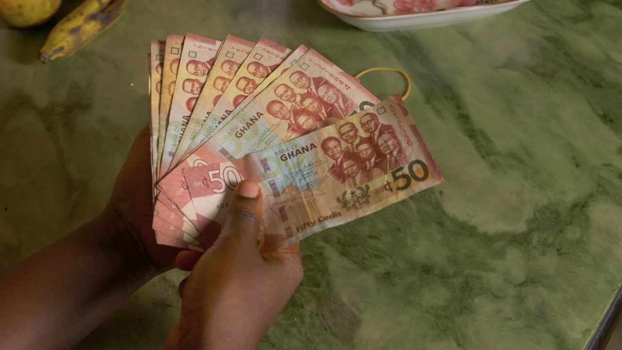 흑인 여성 아프리카 여성은 그녀의 손에 가나의 통화인 지폐를 들고 있습니다.