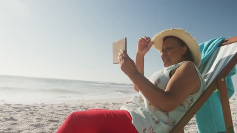 smiling senior african american woman lying on sunbed and reading book on sunny beach