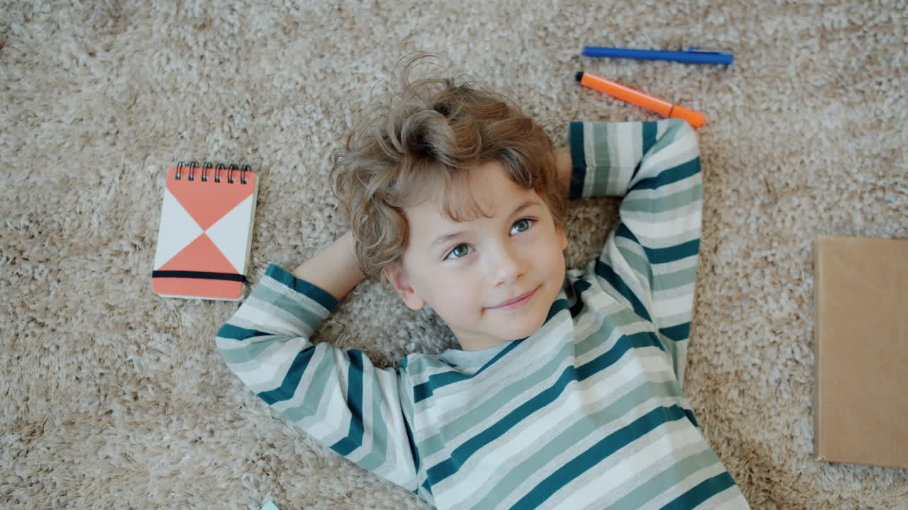 Happy Boy Relaxing on the Carpet with School Supplies