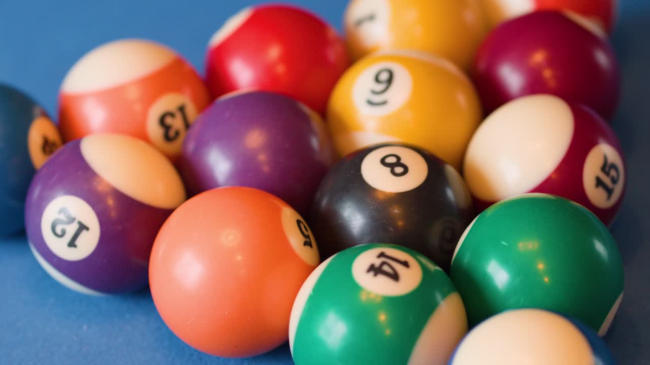 Billiard balls roll and slow on blue felt table, natural lighting, shallow depth of field