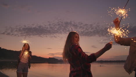 un grupo de amigos de hombres y mujeres alegres celebran las vacaciones en la playa con chispas y fuegos artificiales.