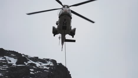 cargo helicopter with lifting cable and load attached landing in the difficult-to-reach mountainous terrain