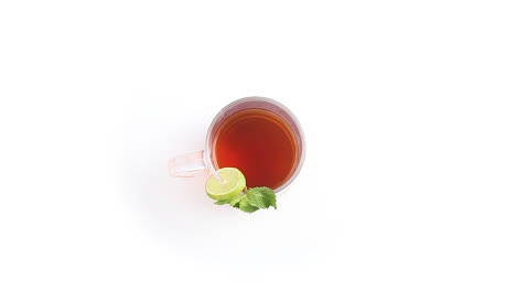 Té-De-Limón-En-Una-Taza-De-Vidrio-Transparente-Con-Hojas-De-Menta-De-Limón-En-Rodajas-En-Un-Plano-Lateral-Giratorio-De-Fondo-Blanco