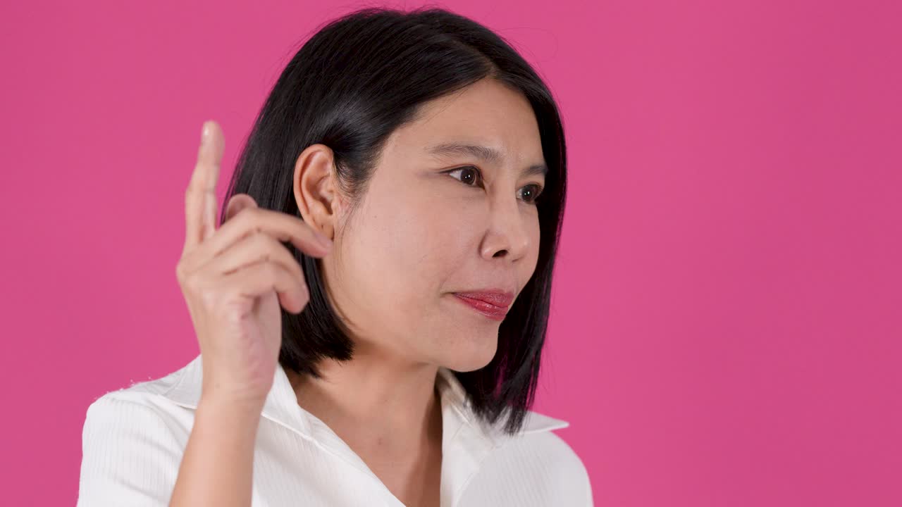 Inquadratura media di una donna asiatica che parla e indica con il dito su uno sfondo rosa