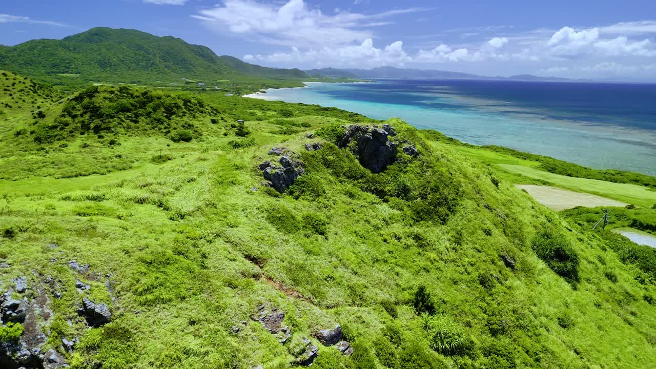 Korkealta kuvattu dronekuvamateriaali liukuu yli vehreiden, kivisten rinteiden paljastaen Ishigakin saaren, Okinawan, Japanin upean rannikon, smaragdinvihreät laguunit ja kaukaiset vuoret.