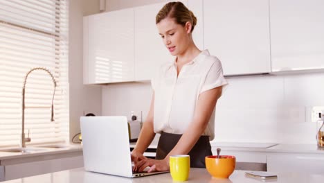 mujer usando una computadora portátil mientras desayuna en la cocina