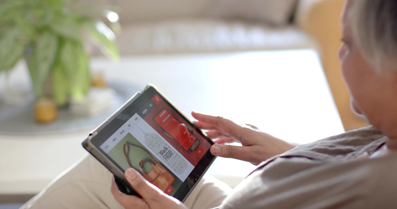 Senior African American woman on sofa tapping tablet QR-code after spotting bag listing, copy space
