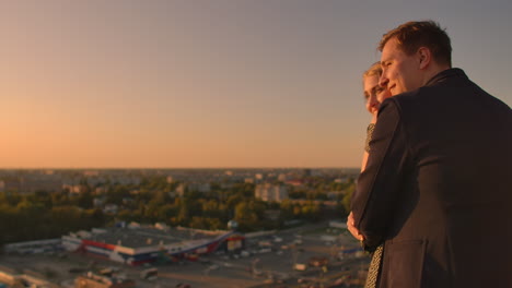 encantadora dulce felicidades pareja sentarse en el techo con increíble vista de la puesta de sol en la ciudad urbana ciudad. se aman abrazos muy ternura sol va entre el cabello