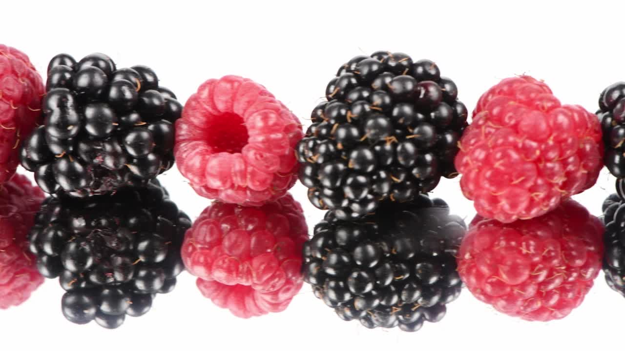 las frambuesas se alternan con las moras negras. movimiento de izquierda a derecha en el espejo plateado. vista lateral. movimiento en bucle. rotación 360.