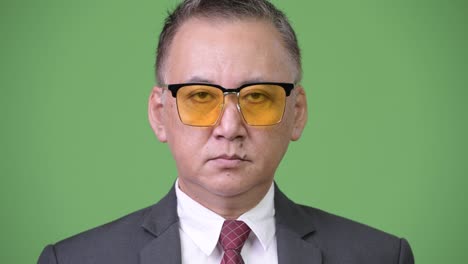 un hombre de negocios japonés maduro con gafas de sol contra un fondo verde.