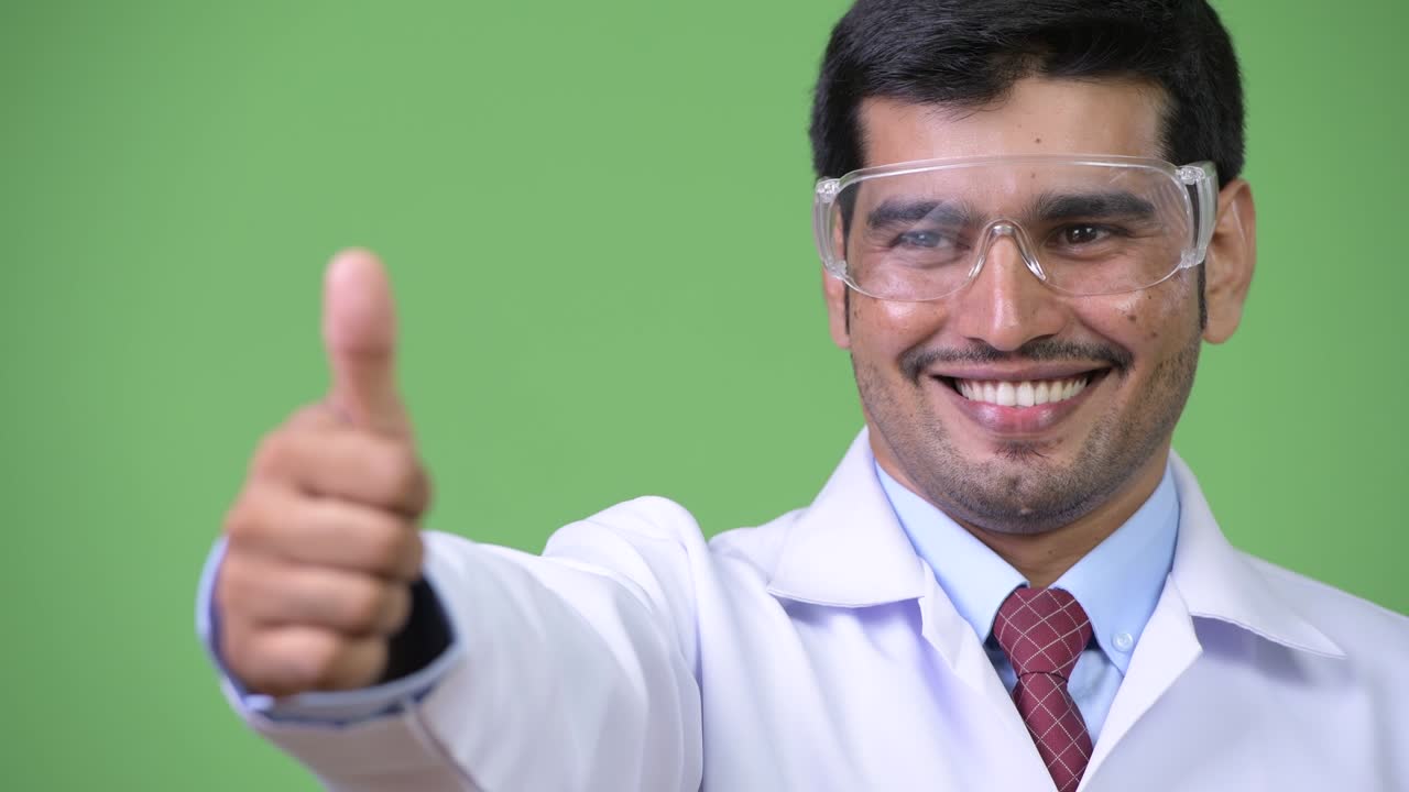 Young handsome Persian man doctor wearing protective glasses giving thumbs up
