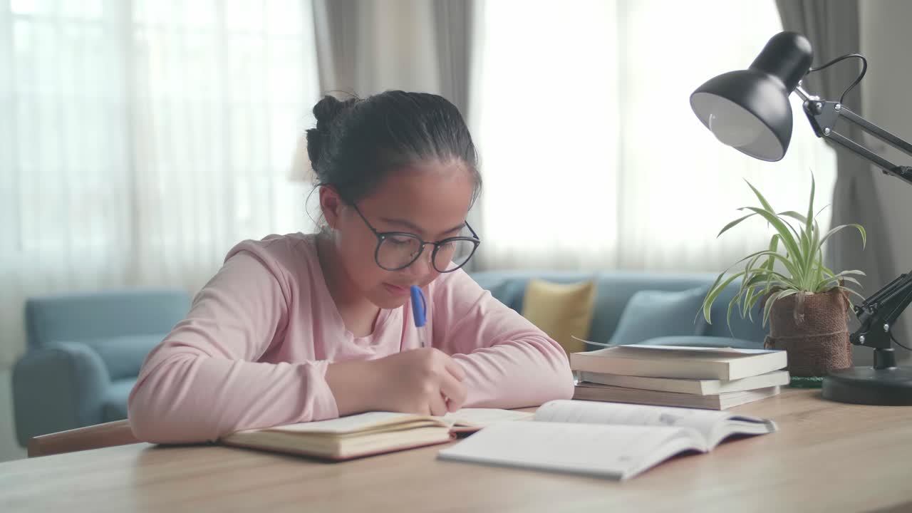 Asian Girl Is Studying At Home, Asia Child Writing While Sitting On The Table At Living Room