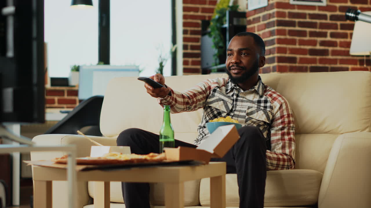 African american man eating chips in bowl at home