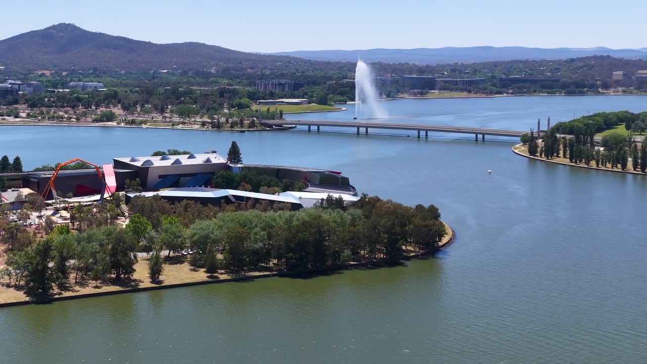Amplia panorámica aérea con dron sobre un lago soleado con una gran fuente de agua y paisaje urbano