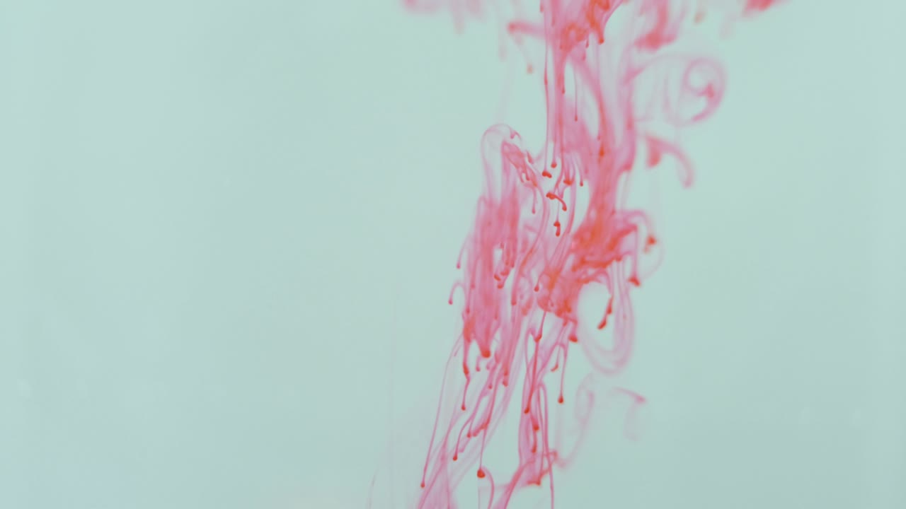 el tinte rojo cae a través de un líquido transparente con espacio blanco negativo creando un retrato abstracto de caos y movimiento