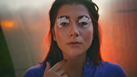 modelo de moda tocando la cara en un primer plano de luz naranja posando con pestañas de pétalos.