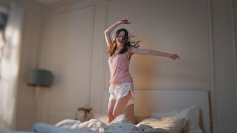 happy teenager jumping bed in headphones. carefree girl listening energetic song