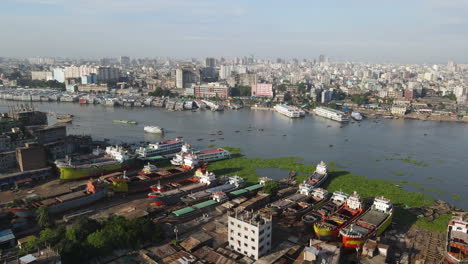 aerial: shipyard at buriganga river bank with vast cityscape - drone flying forward shot