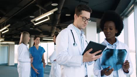 close-up view of caucasian male doctor typing on tablet and discussing xray scan with african american female doctor in hospital