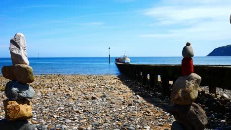 colourful rocks arrangement balanced on sunny llandudno beach seaside shoreline dolly right alongside pier