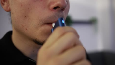 close up shot of a young man using a tobacco heating device in the house