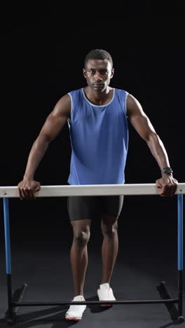 vertical video: african american male athlete holding onto horizontal hurdle, black background