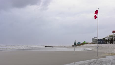 Double-red-flags-blowing-in-strong-wind-with-large-waves-on-a-beach