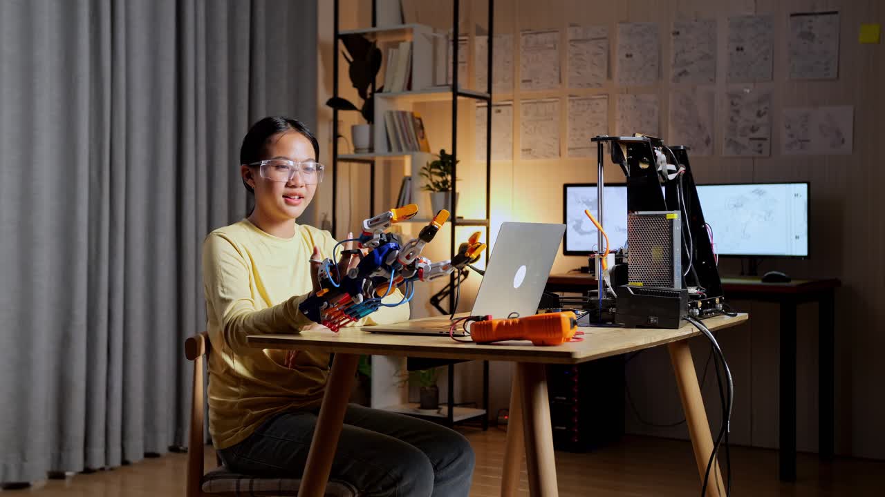 집에서 노트북으로 작업하는 동안 카메라에 미소 짓는 사이보그 손을 가진 십대 아시아 소녀