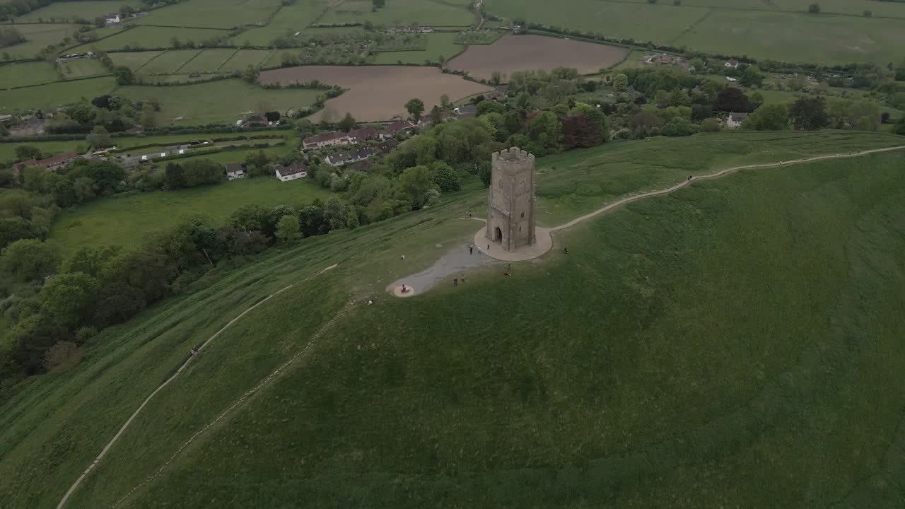 Aerial view of Glastonbury, drone rotating and camera facing down over the Glastonbury Tor, drone rotating to the left showing the st Michaels tower and the houses around the Tor. 4K, 60fps.