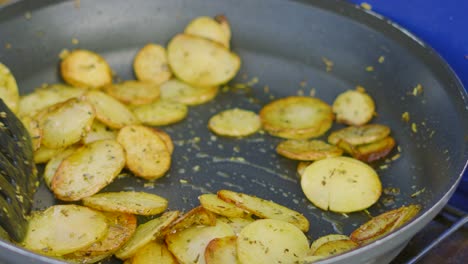 crispy potatoes with seasoned herbs de provence and olive oil being turned in very hot frying pan being cooked outside on summer evening 4k