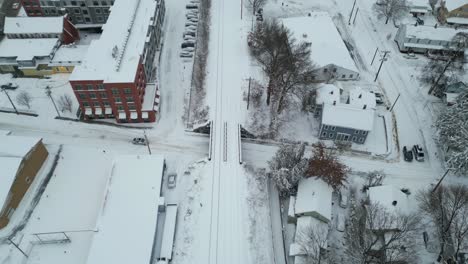 Bird's-eye-view-tilt-down-as-car-drives-below-snow-covered-railroad-tracks-on-icy-road