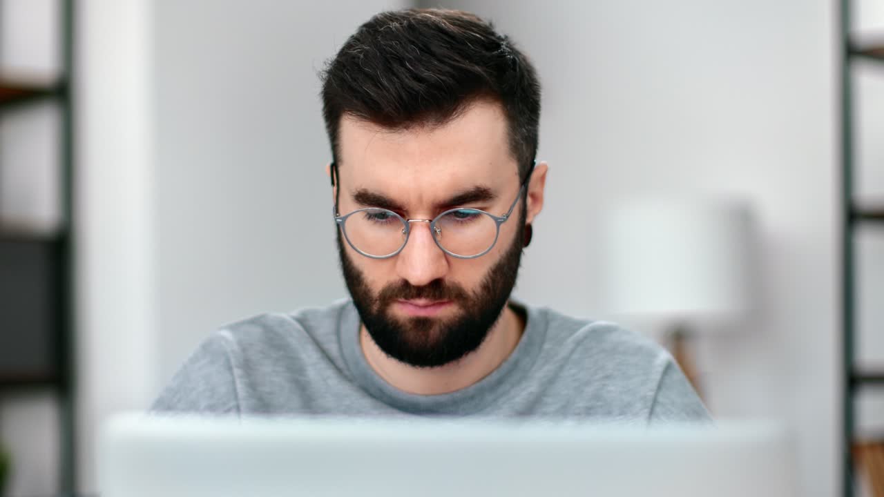 primer plano hombre confiado con gafas trabajando en una computadora portátil navegando por internet en una oficina doméstica moderna