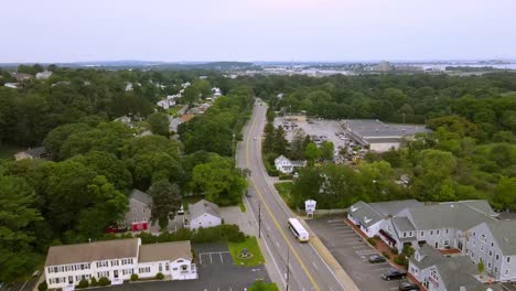 Luftaufnahme-über-Autos,-Die-Auf-Der-Lincoln-Street-Inmitten-Des-Wunderschönen-Grüns-Von-Hingham-Town,-Massachusetts,-Fahren