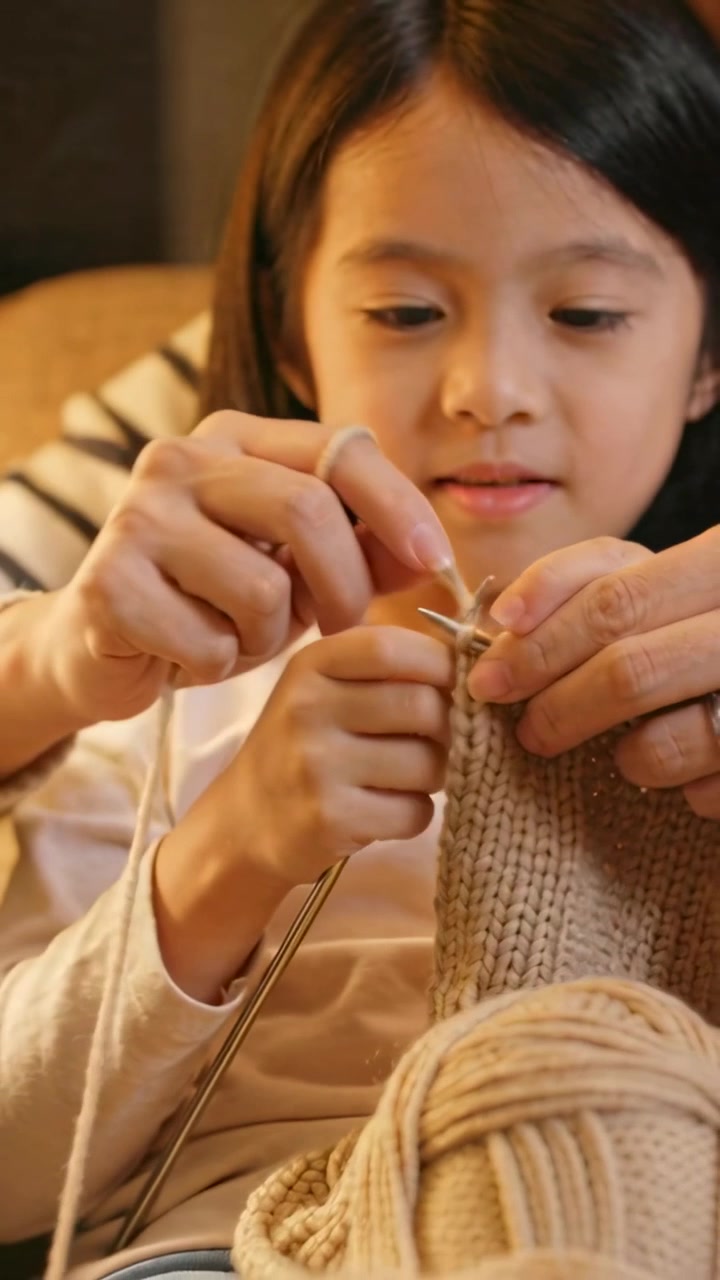 Video vertical: Manos de adulto guiando a un niño que aprende, insertando una aguja y envolviendo hilo en un sofá