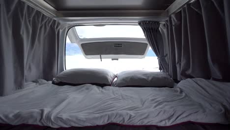 Interior-of-motorhome-bed-with-pillows-and-blankets-by-Lake-Wakatipu,-Queenstown,-New-Zealand-with-snowcapped-mountains-in-background