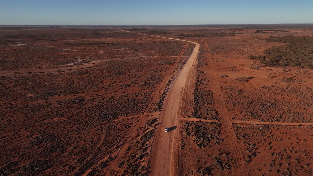 Ampia vista panoramica aerea di strada sterrata tortuosa e auto che scompare nel paesaggio desertico rosso all'ora d'oro, natura selvaggia australiana