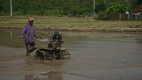 farmer operating a power tiller in a muddy rice paddy