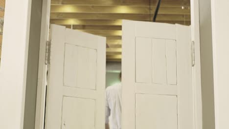 Man-entering-white-double-doors.-Sign-above-the-doorways.-Man-open-doorway