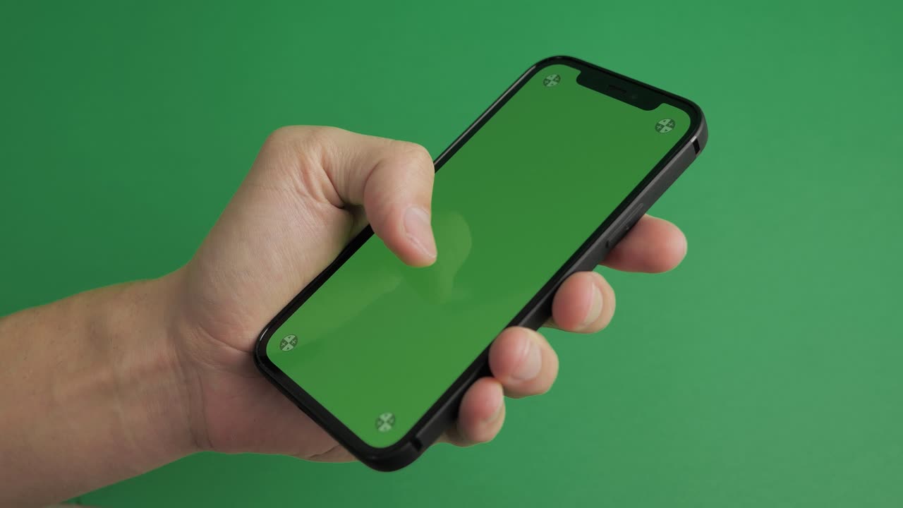 primer plano de mano masculina sosteniendo teléfono móvil con pantalla verde vertical clave de croma tecnología de teléfono inteligente teléfono celular pantalla de mensaje táctil mano sobre fondo verde.