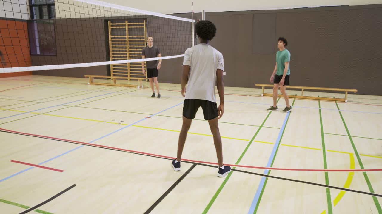 Diverse male teammates reacting to ball from left, blocking and redirecting at net during practice