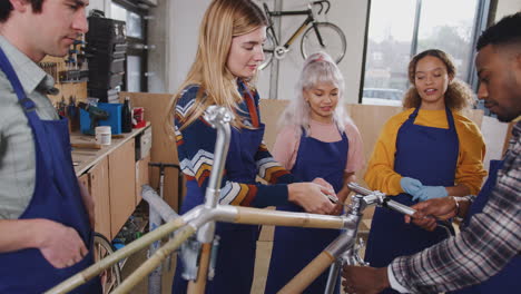 multi-cultural team of trainees in workshop learn how to assemble hand built bicycle frame together